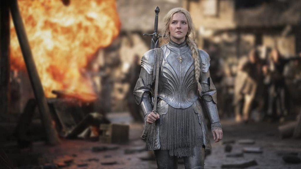 Seasons 3-5 of The Lord of the Rings: The Rings of Power- Galadriel walking in her silver armor with a large burst of fire and people in the background. Seasons 3-5 of The Lord of the Rings: The Rings of Power- Galadriel walking in her silver armor with a large burst of fire and people in the background.