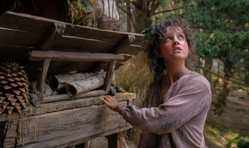 The Lord of the Rings: The Rings of Power- Nori, a curious Harfoot, looking up into the sky as she approaches a wooden cart full of scrolls. The Lord of the Rings: The Rings of Power- Nori, a curious Harfoot, looking up into the sky as she approaches a wooden cart full of scrolls.